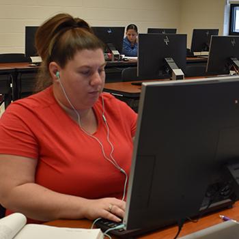 计算机实验室里的女学生戴着耳机，学生在电脑前
